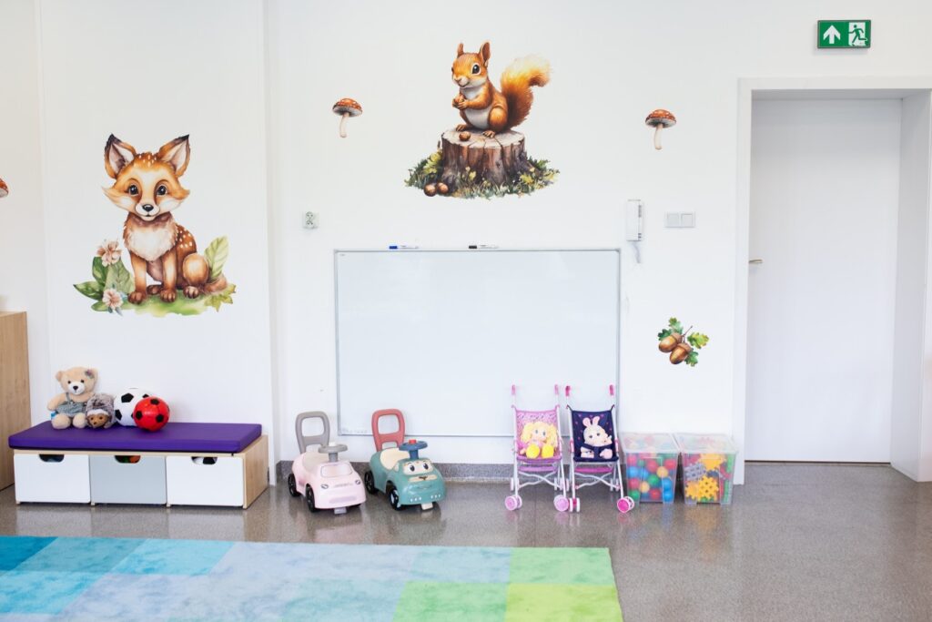 Kolorowa sala w żłobku w Będzinie Zaczarowany Las - zabawki, jeździki, pluszaki i dekoracje ze zwierzętami na jasnej ścianie.